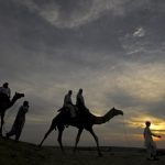 File photo of tourists riding camels as they are silhouetted against the setting sun over the Thar Desert at Sam village