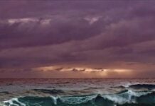 Dramatic sunset over a choppy sea with a glowing horizon and large curling waves in the foreground.