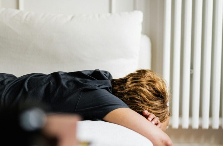 Person lying face down on a light sofa with one arm hanging toward the wooden floor, resting.