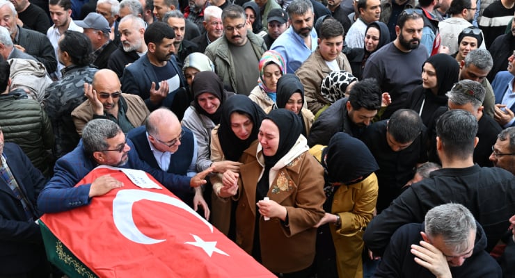 Crowd of mourners surrounding a coffin draped with a Turkish flag at a funeral ceremony.