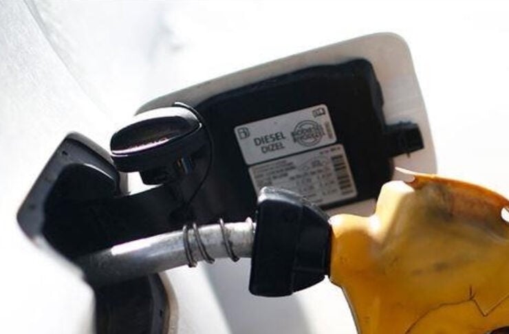 Close-up of a diesel pump nozzle inserted into a white car's fuel tank.