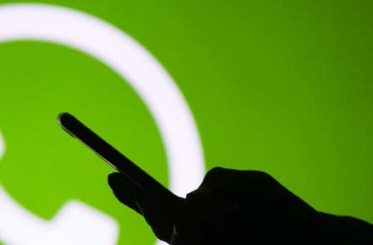 Silhouette of a hand holding a smartphone with a large WhatsApp logo in a bright green background.