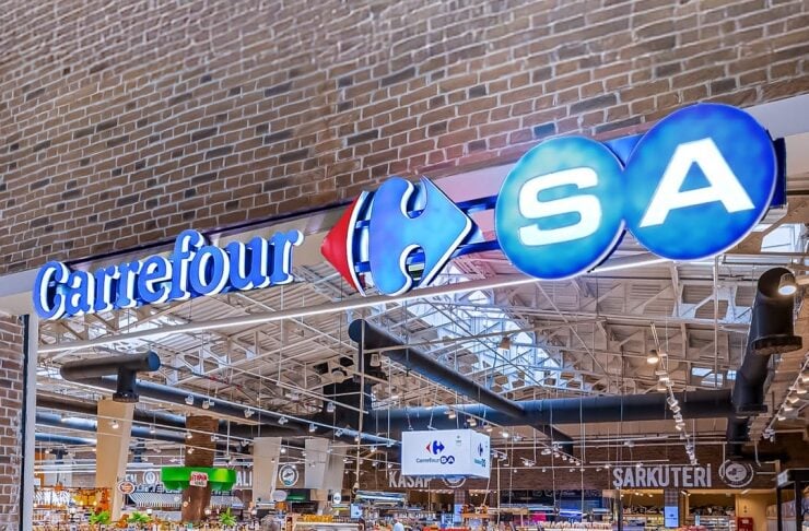 CarrefourSA supermarket interior with colorful fruit and vegetable displays in the foreground and a red delivery vehicle on display.