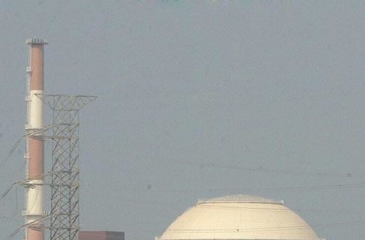 Industrial power plant with a large white domed building and a tall smokestack against a clear sky