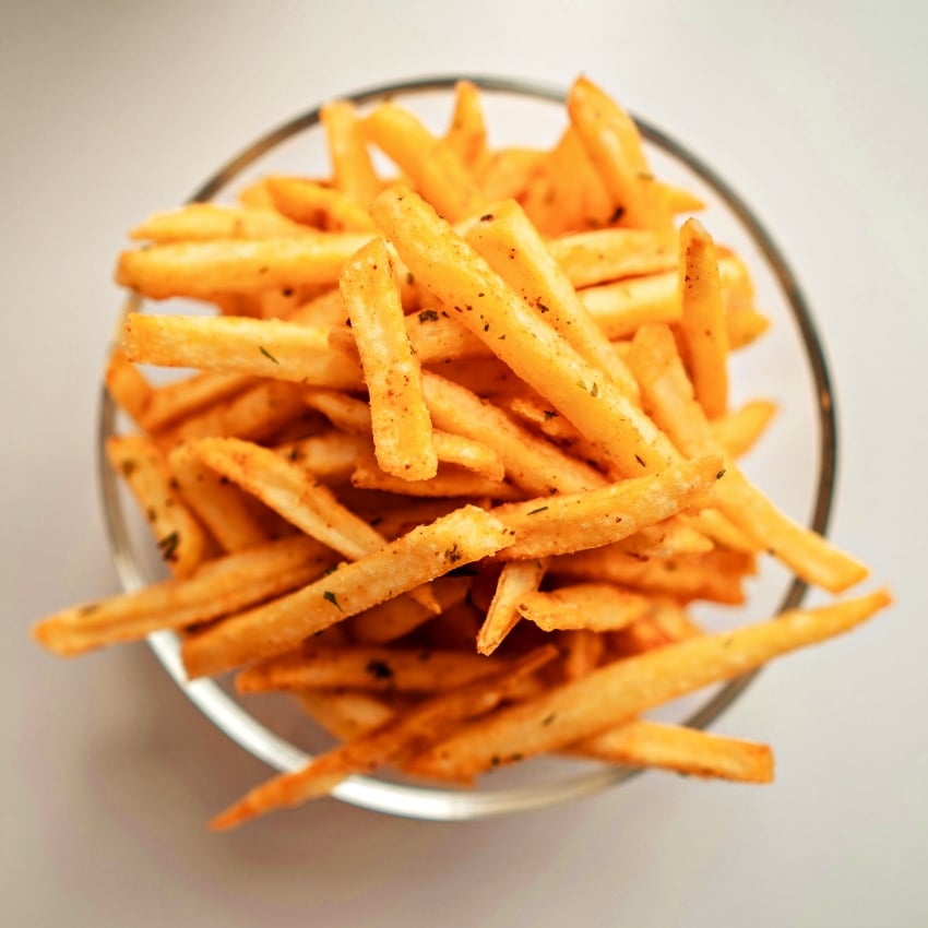 Golden french fries sprinkled with herbs in a metal bowl, viewed from above