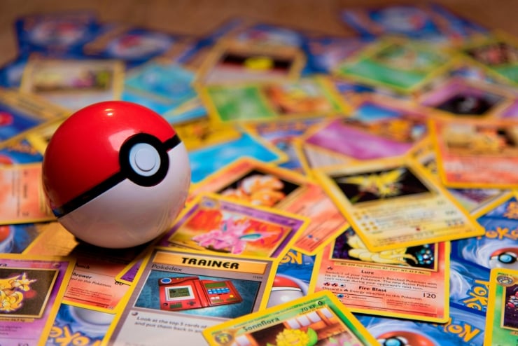 Red and white Poké Ball on top of scattered Pokémon trading cards on a colorful surface.
