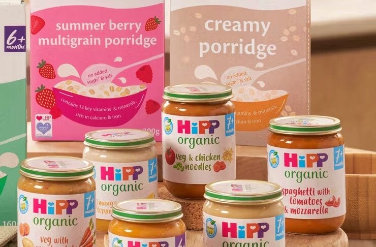 Assorted HiPP organic baby food jars on a round wooden board with berry porridge boxes in the background.