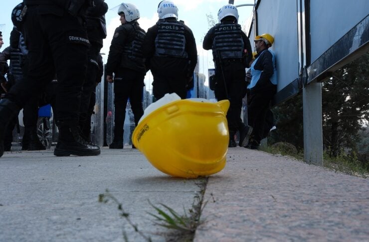 Yellow safety helmet lies on the sidewalk in the foreground as police officers in riot gear stand behind in the background.