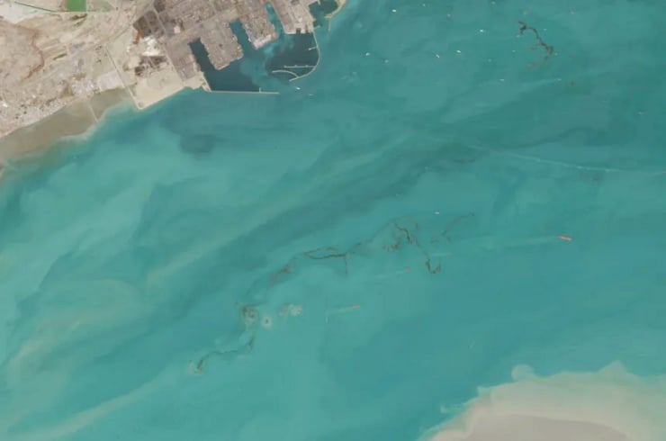 Aerial view of a coastline with turquoise seawater, sandy beach, and harbor piers along the shore.