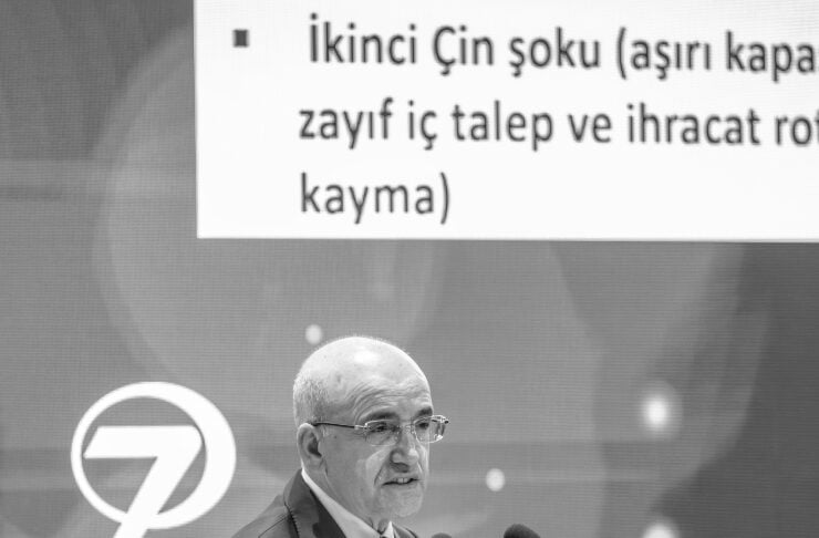 Man in a suit speaking at a podium with two microphones, a Turkish slide backdrop, and a kanall logo behind him.