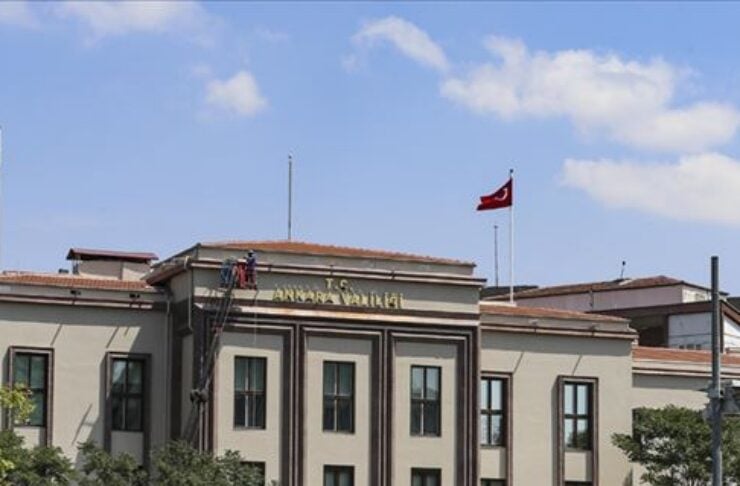 Facade of a Turkish government building with a flag on top and trees in front.