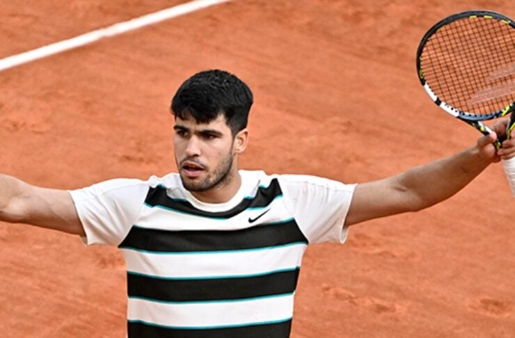 Tennis player on a clay court with arms outstretched, holding a racket in one hand.