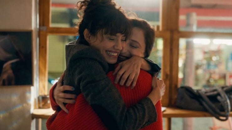 Two friends share a warm hug and smile in a cozy cafe setting.