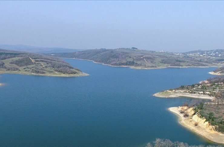 Aerial view of a winding blue lake with sandy cliffs and brown hills in the distance.