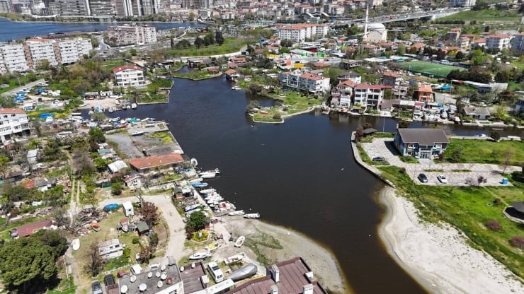 Aerial view of a suburban waterfront neighborhood with a winding dark waterway, boats along the shore, and scattered houses and green spaces.