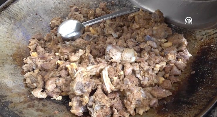 Chopped browned beef cooking in a large frying pan with a metal ladle resting on top.
