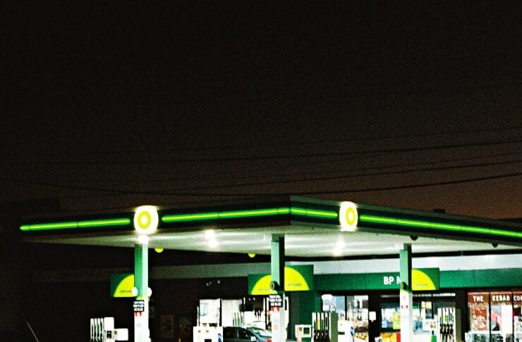 Nighttime BP gas station with bright green and yellow branding, pumps under a lit canopy and a car at a pump in the foreground.