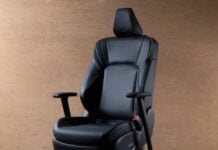 Ergonomic black leather office chair with headrest and caster wheels on a wooden floor base.