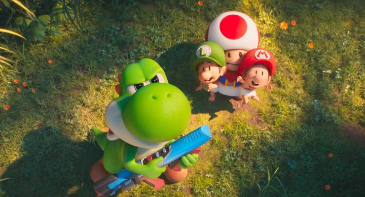 Yoshi holds a blue toy blaster while Mario, Luigi, and Toad stand behind on sunlit grass, looking up at the camera.