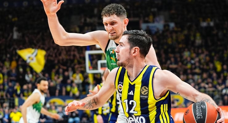 Basketball player in blue-yellow jersey (#12) dribbles toward the basket while a defender in green reaches in.