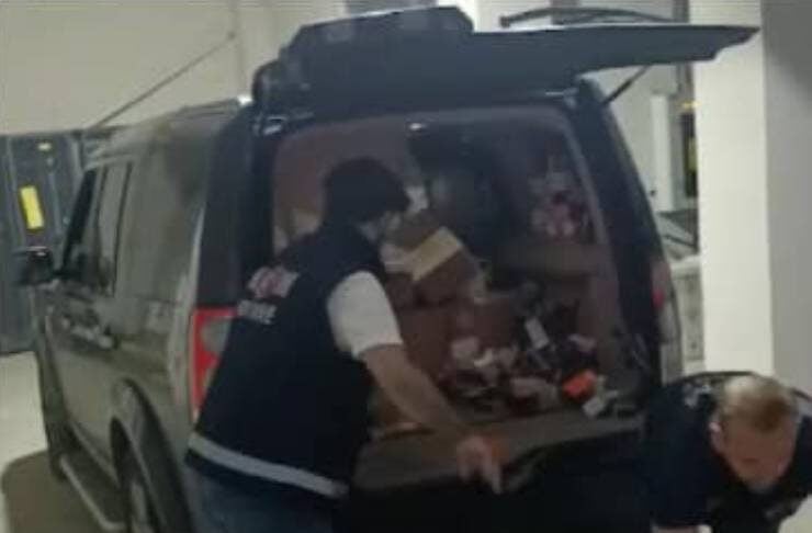 Two workers unload cardboard boxes from the back of a dark van in a garage.