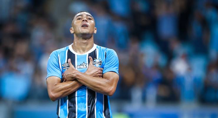 Soccer player in a blue and black striped jersey crosses arms over the chest and gazes upward on the field.