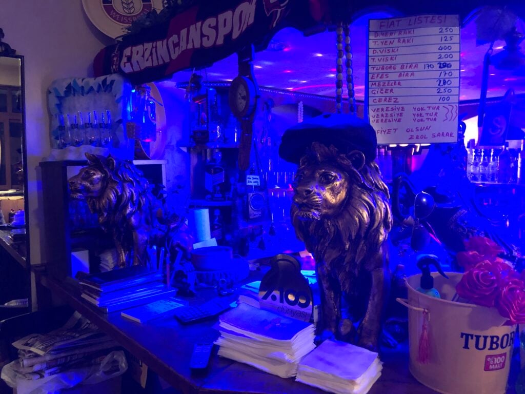 Bar counter with two bronze lion statues under blue lighting; a handwritten menu on a whiteboard and shelves of bottles behind.