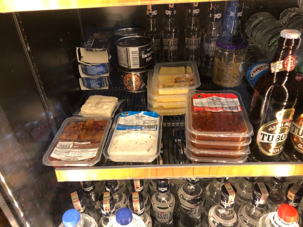 Assorted ready-to-eat packaged dishes in a refrigerated display, including meat stews and a white sauce tray, with beer bottles on the right.