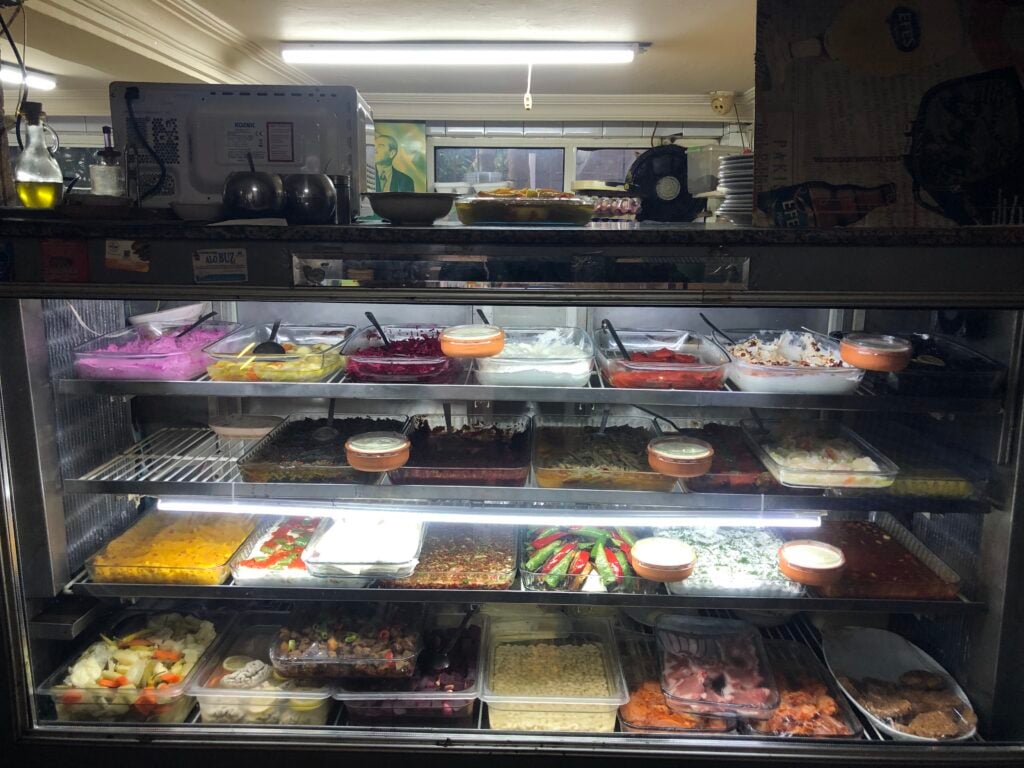 Glass-front deli counter filled with trays of colorful prepared foods and salads, with lids and scoops visible behind the glass glass wall.