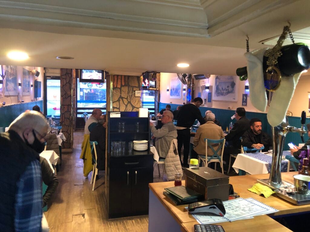 Busy casual restaurant interior with diners at tables, a server in the back, and beer taps on the bar in the foreground.