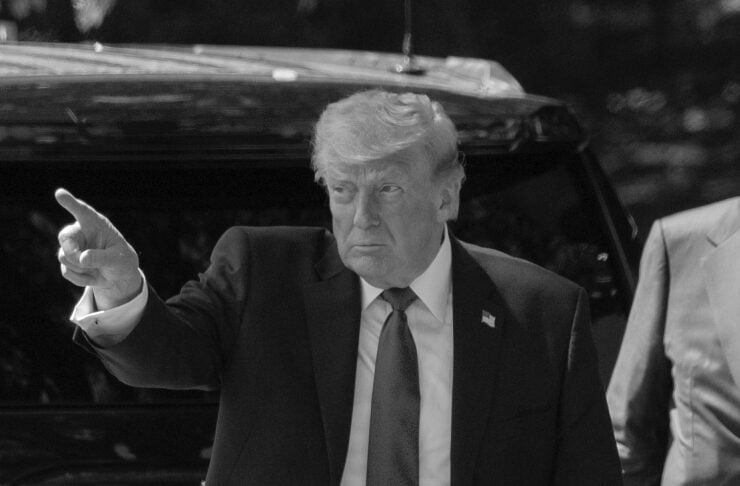 Man in a dark suit points with his arm extended while stepping from a black SUV.