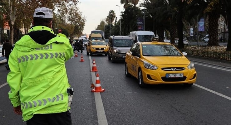 Traffic officer in a neon jacket directing cars on a city street with orange cones and yellow taxis nearby.