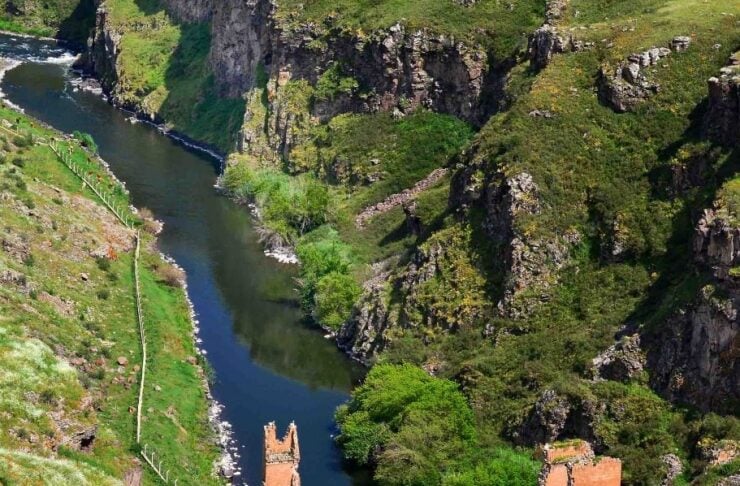 River winds through a rocky ravine with partially submerged red-brick ruins on the banks.