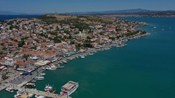 Aerial view of a coastal town with red-tiled roofs along a harbor and boats docked at the waterfront.