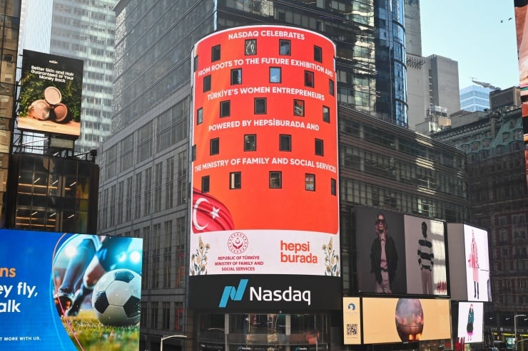Cylindrical red digital billboard in a busy city square advertising Turkey’s women entrepreneurs, with a Nasdaq sign beneath it.