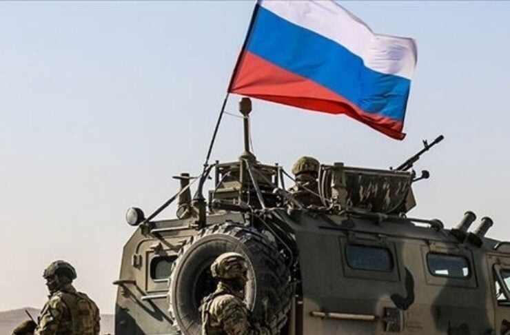 Armored military vehicle with soldiers and a waving Russian flag in a desert setting.