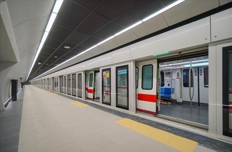 Empty underground subway platform with a long train stopped at the station; doors are open and red stripe accents run along the cars.