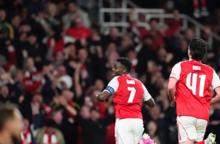 Arsenal players with numbers 7 and 41 celebrate or run on the pitch while the goalie sits on the grass and a crowded stadium watches in the background.
