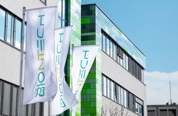 Modern office building with a green-tiled corner and three white flags with teal vertical text.