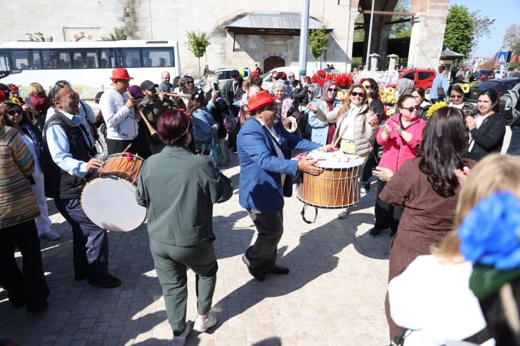 A lively street festival with people dancing and playing large drums while a crowd applauds nearby.