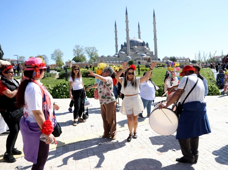 Group of people dancing in a sunny plaza as a drummer watches, with a large domed mosque and four minarets in the background.