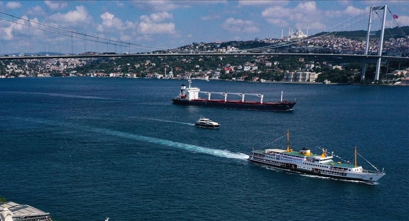 A large white and yellow passenger ferry sails in a blue bay with a suspension bridge and hillside city in the background.