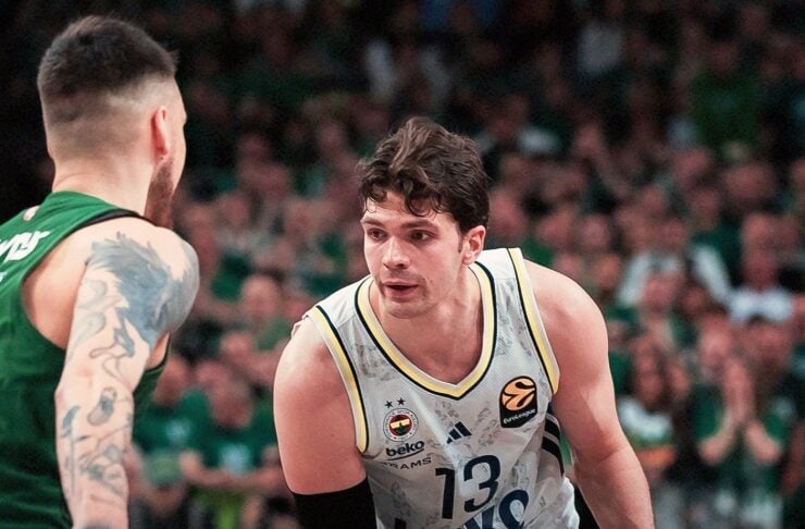Basketball player in a light jersey with number 13 dribbles the ball while defended by a player in green on a crowded court.