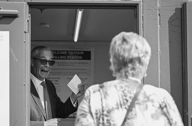 Election worker in a suit hands a ballot to a voter at the doorway of a polling station.