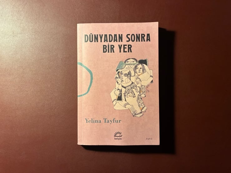 Pink paperback book cover reading 'DÜNYADAN SONRA BİR YER' by Yelina Tayfur with an abstract illustration on a brown surface.