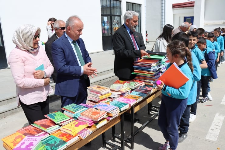 Officials give colorful books to children lined up at a book donation event outside a school outside.