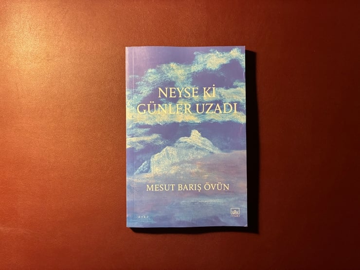 Blue book cover with clouds and mountains; title 'Neyse ki Günler Uzadı' by Mesut Barış Övün (author name may vary in spelling).