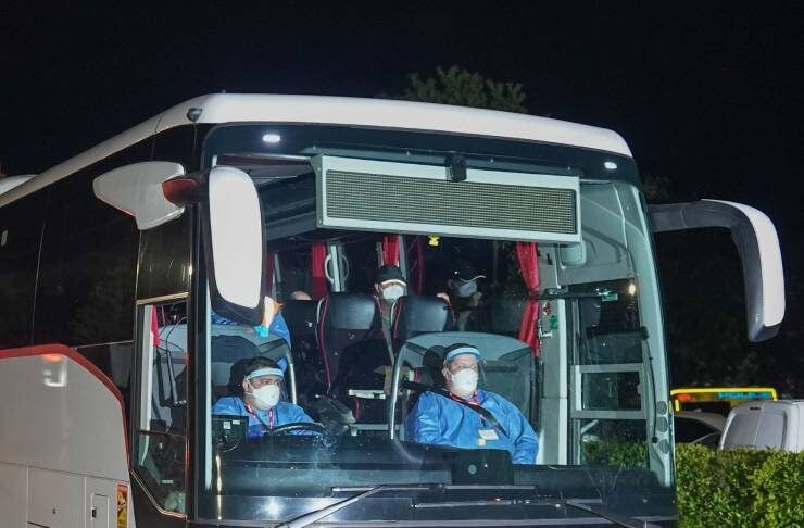 Nighttime view of a white Mercedes tour bus with passengers wearing face masks visible through the windshield.