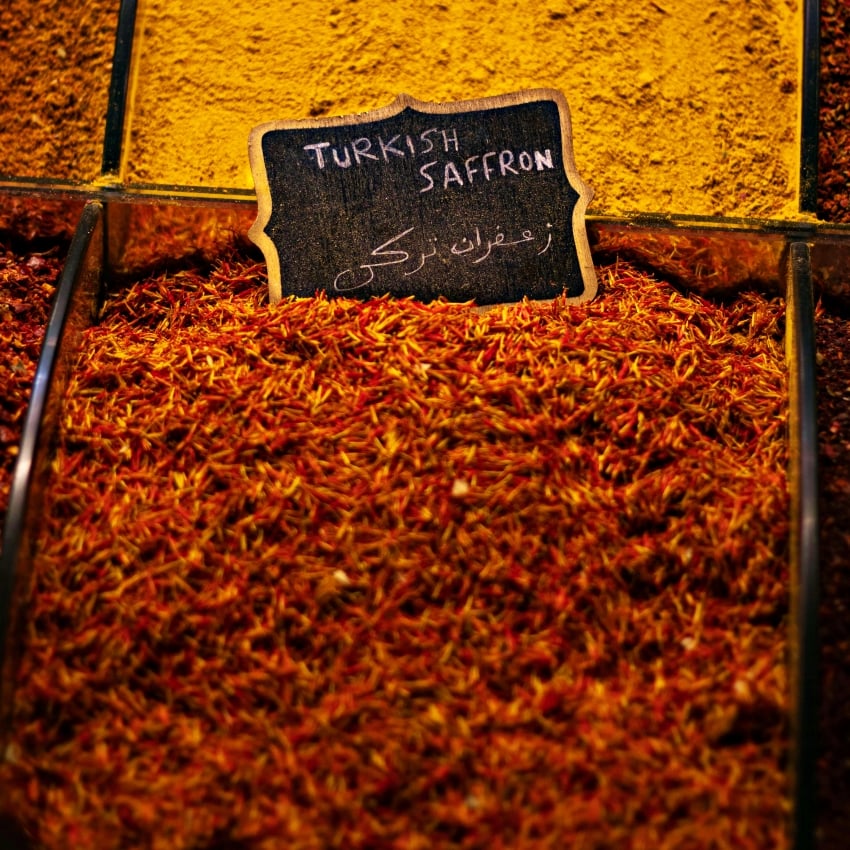 Pile of Turkish saffron threads in a market display with a chalkboard sign reading Turkish Saffron.
