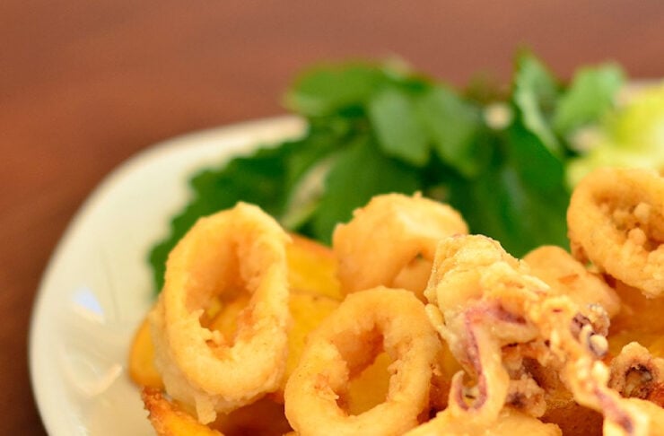 Plate of golden fried calamari rings and potato wedges with a parsley garnish on a white plate.